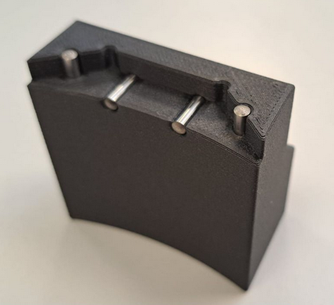 schwarzes 3D gedrucktes Bauteil aus Kohlefaserverstärktem Kunststoff versehen mit Pins aus gehärtetem Stahl. Hybrides 3D Druck Bauteil